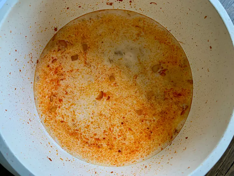 Simmering red curry broth with coconut milk and water in a pot.