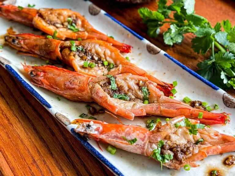 Butterfly shrimp with garlic and soy glaze served on a rectangular plate, topped with chopped cilantro and scallions.