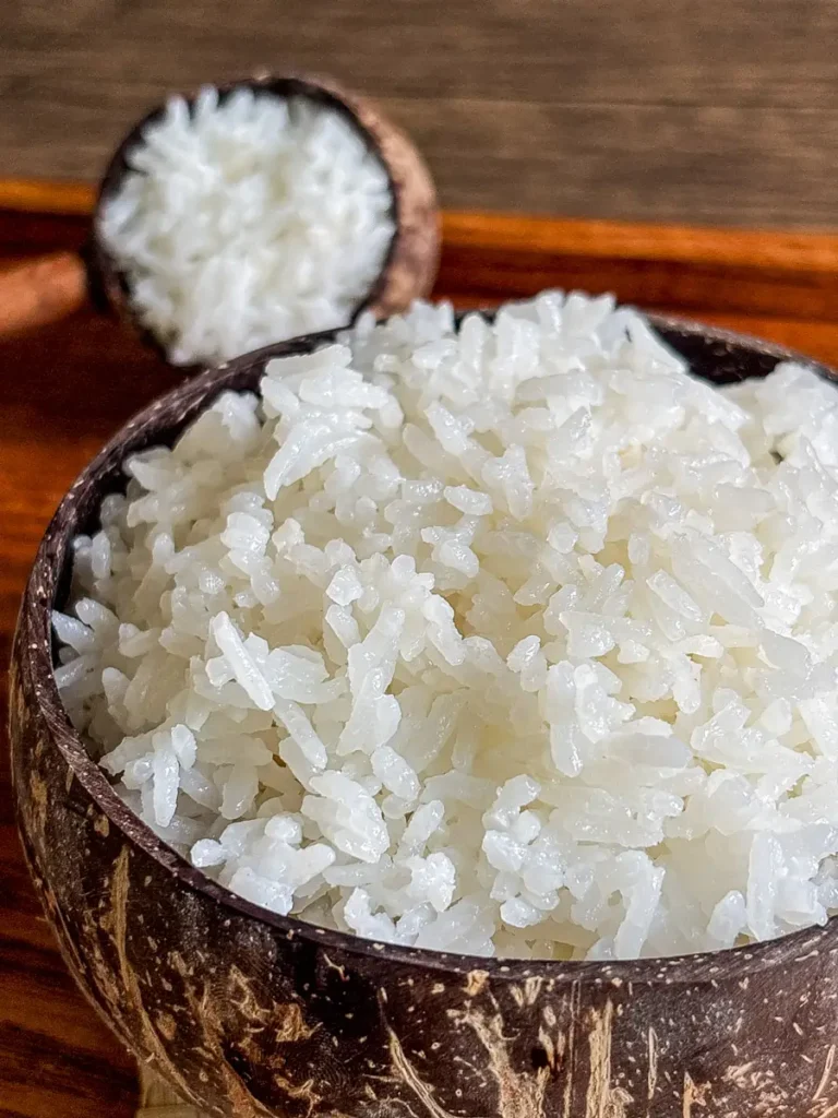 Thai coconut jasmine rice in a coconut shell bowl placed on a woven mat with a wooden table background.