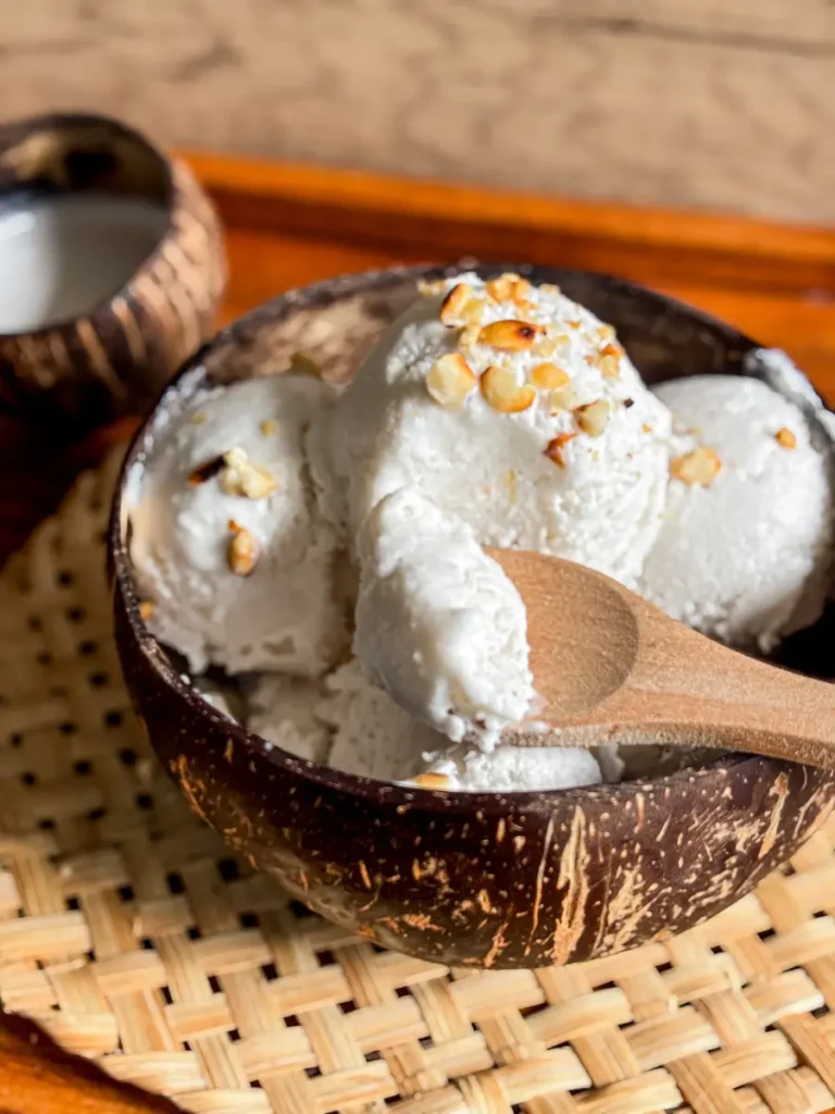Creamy coconut milk ice cream topped with roasted peanuts, served in a coconut bowl with a wooden spoon.