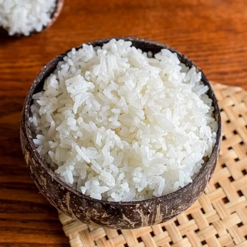 Thai coconut rice served in a natural coconut bowl, with a wooden spoon of rice in the background.
