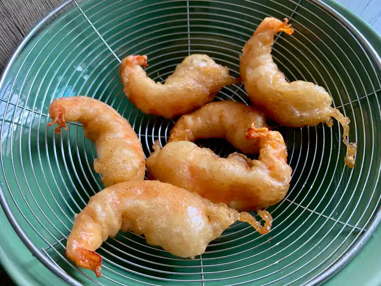 Freshly fried shrimp tempura draining on a wire rack over a green bowl.