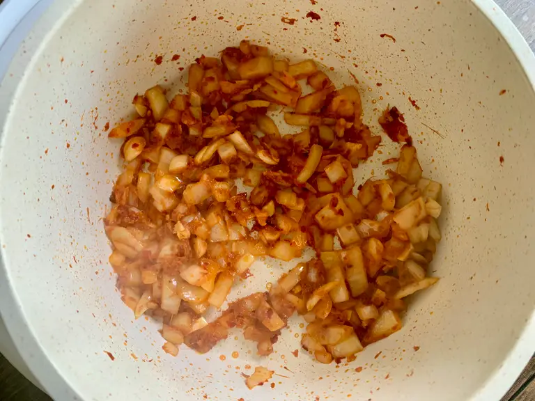 Chopped onions and Thai red curry paste frying together in a pot.