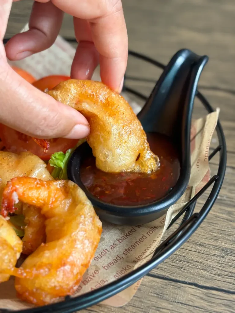 Hand dipping crispy shrimp tempura into a sweet chili dipping sauce.