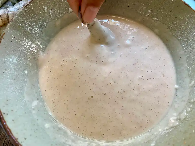 Shrimp being dipped into cold tempura batter in a mixing bowl.