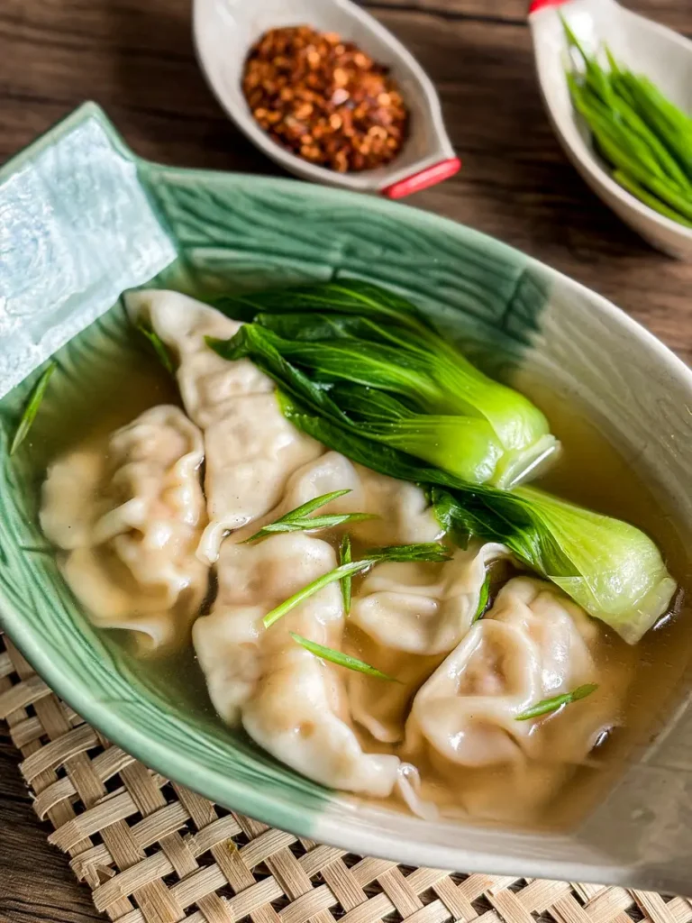 Close-up of Thai wonton soup with bok choy in a light broth, garnished with green onion.