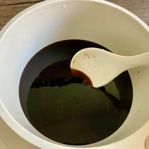 Thai stir fry sauce simmering in a white saucepan with a white ceramic spoon used for stirring.