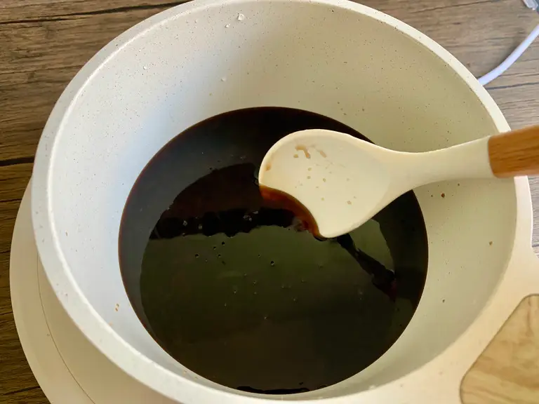 Thai stir fry sauce simmering in a white saucepan with a white ceramic spoon used for stirring.