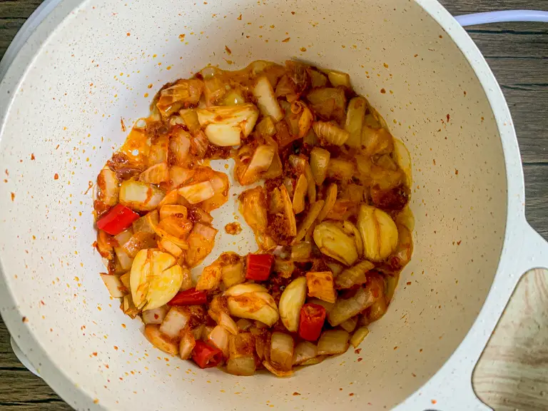 Pasta de curry vermelho adicionada aos aromáticos amolecidos, cozinhando em óleo até ficar perfumada.