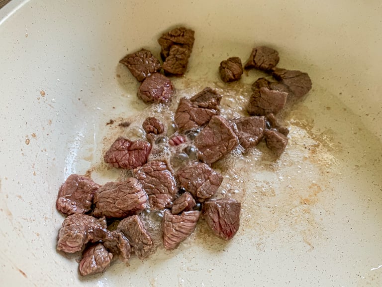 Pedaços de carne fervendo em uma frigideira quente enquanto tosta.