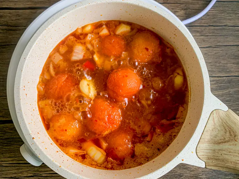 Mistura de sopa de tomate fervendo na panela com superfície borbulhante e pedaços visíveis.