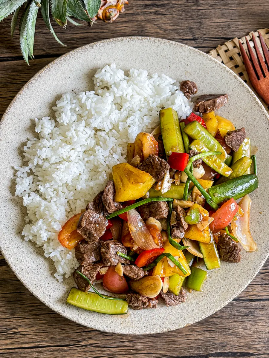 Sweet and sour beef stir fry on a plate with jasmine rice – colorful vegetables, pineapple, and tender beef pieces served on a rustic table.