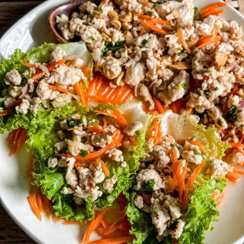 Thai chicken lettuce wraps filled with minced chicken, shredded carrots, and herbs on a white plate.