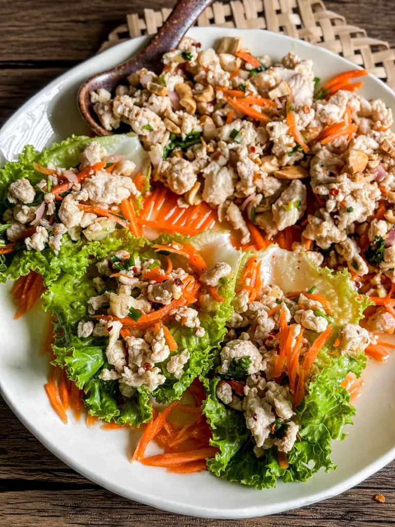 Thai chicken lettuce wraps filled with minced chicken, shredded carrots, and herbs on a white plate.