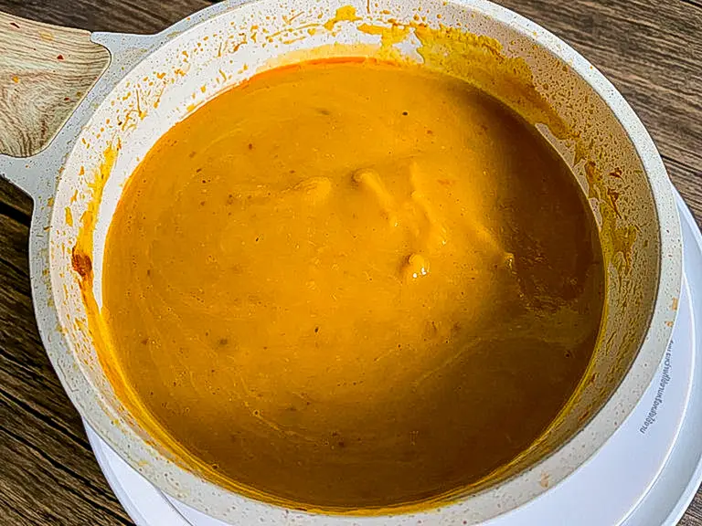 Sopa de abóbora tailandesa suave e cremosa com leite de coco e curry vermelho em uma panela branca.