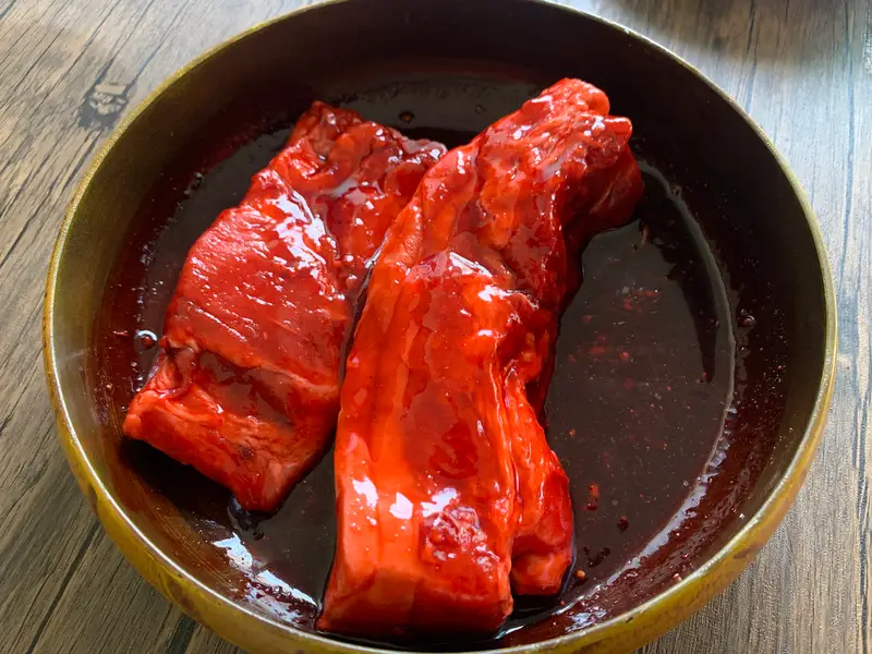 Pork marinating in bright red char siu sauce in a bowl before cooking.