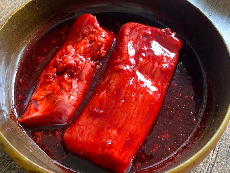Pork tenderloin marinating in red char siu sauce in a bowl before roasting.