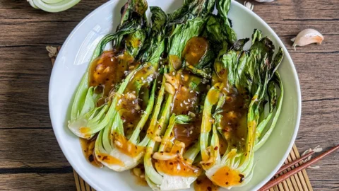 Grilled bok choy with charred leaves and crispy stems served with a savory sauce.