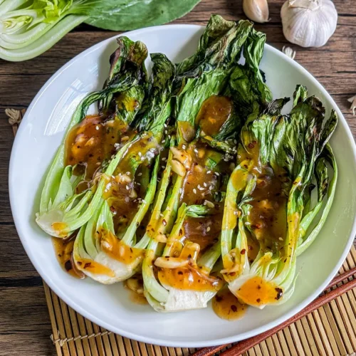 Grilled bok choy with charred leaves and crispy stems served with a savory sauce.