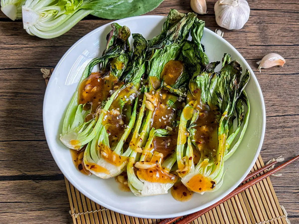 Grilled bok choy with charred leaves and crispy stems served with a savory sauce.