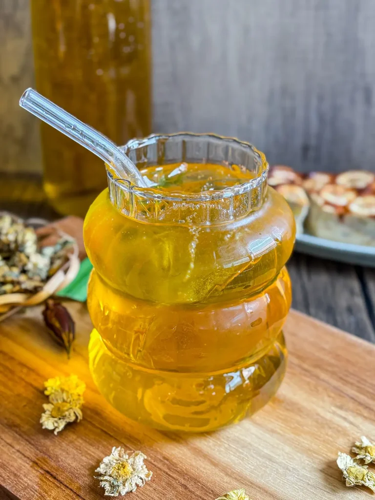 Chilled chrysanthemum tea in a ribbed glass with ice cubes and a glass straw, showing its golden color.