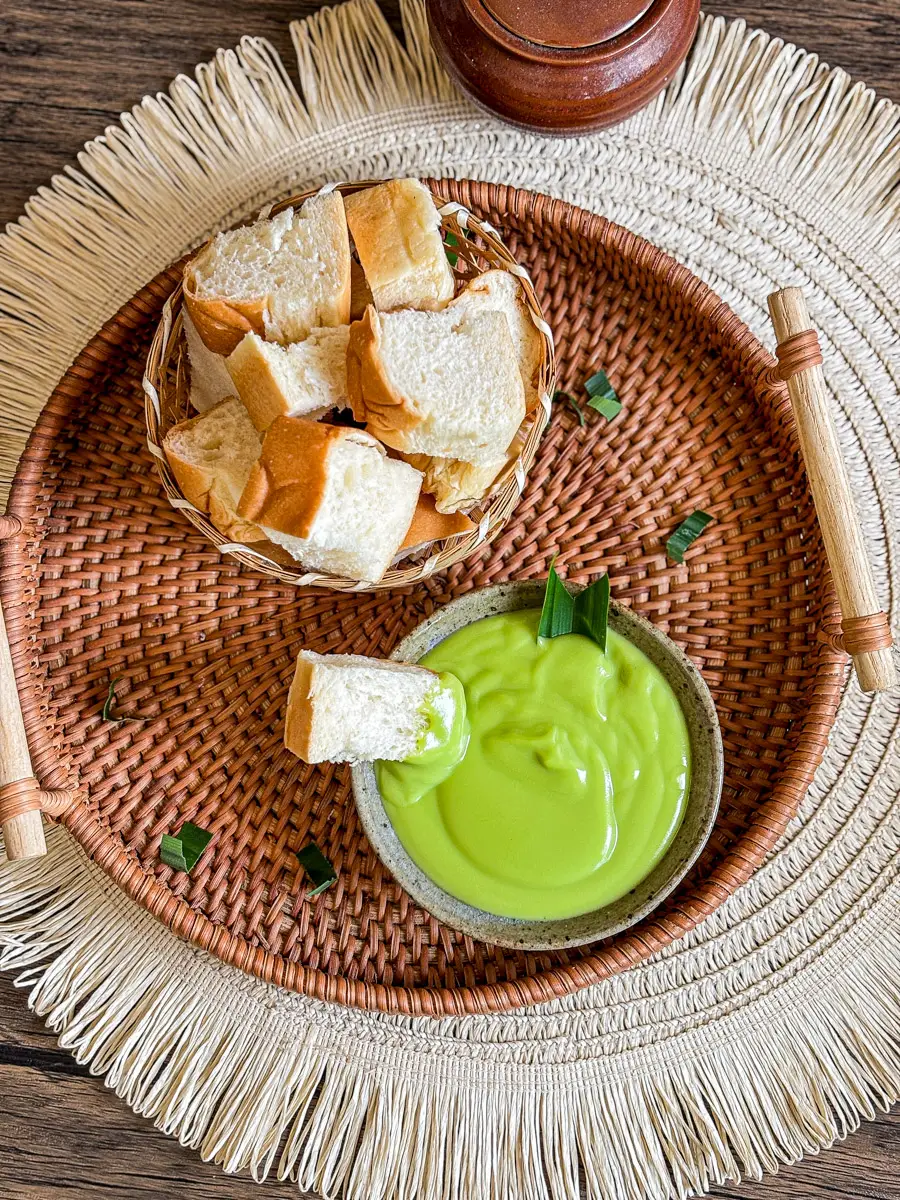 Overhead view of pandan custard (sangkhaya) with bread pieces on a woven tra.