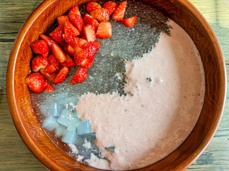 Strawberry sago assembled with cooked sago pearls, coconut milk, fresh strawberries, and jelly cubes in a wooden bowl.