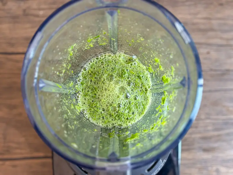 Fresh pandan leaves blended with water in a blender to create a bright green pandan juice base.