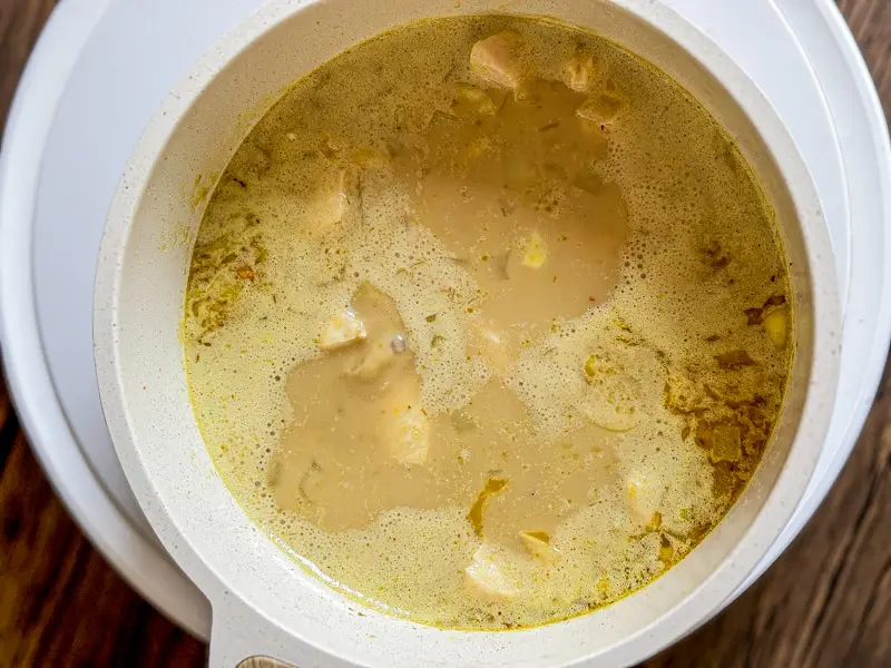 Chicken simmering gently in yellow curry soup until tender and cooked through.