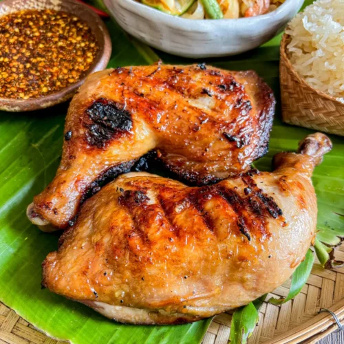 Autêntico frango grelhado tailandês gai yang servido com arroz, salada de mamão e molho picante.