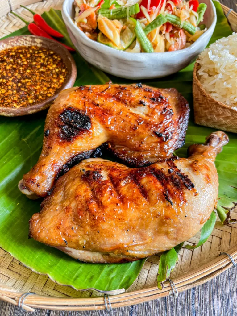 Authentic gai yang Thai grilled chicken served with sticky rice, papaya salad, and spicy dipping sauce.