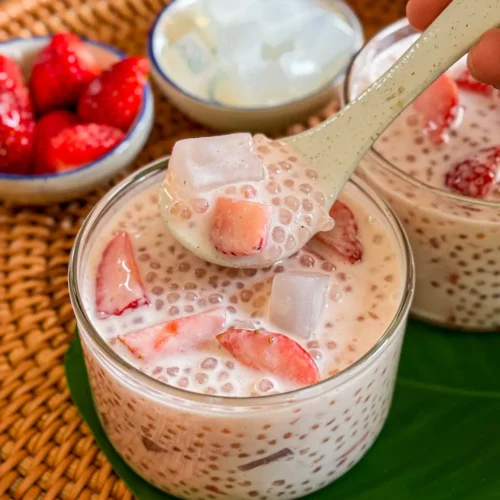 Strawberry sago dessert with coconut milk, translucent sago pearls, fresh strawberries, and jelly cubes scooped with a spoon.