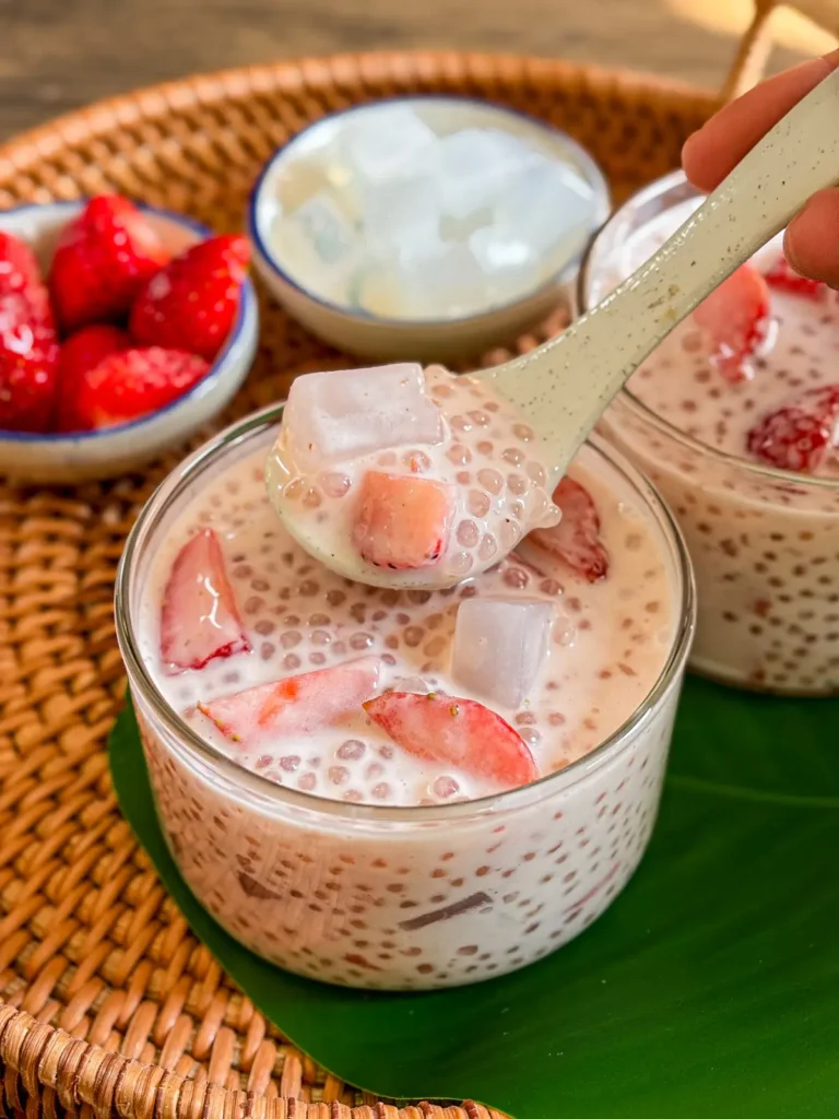 Strawberry sago dessert with coconut milk, translucent sago pearls, fresh strawberries, and jelly cubes scooped with a spoon.
