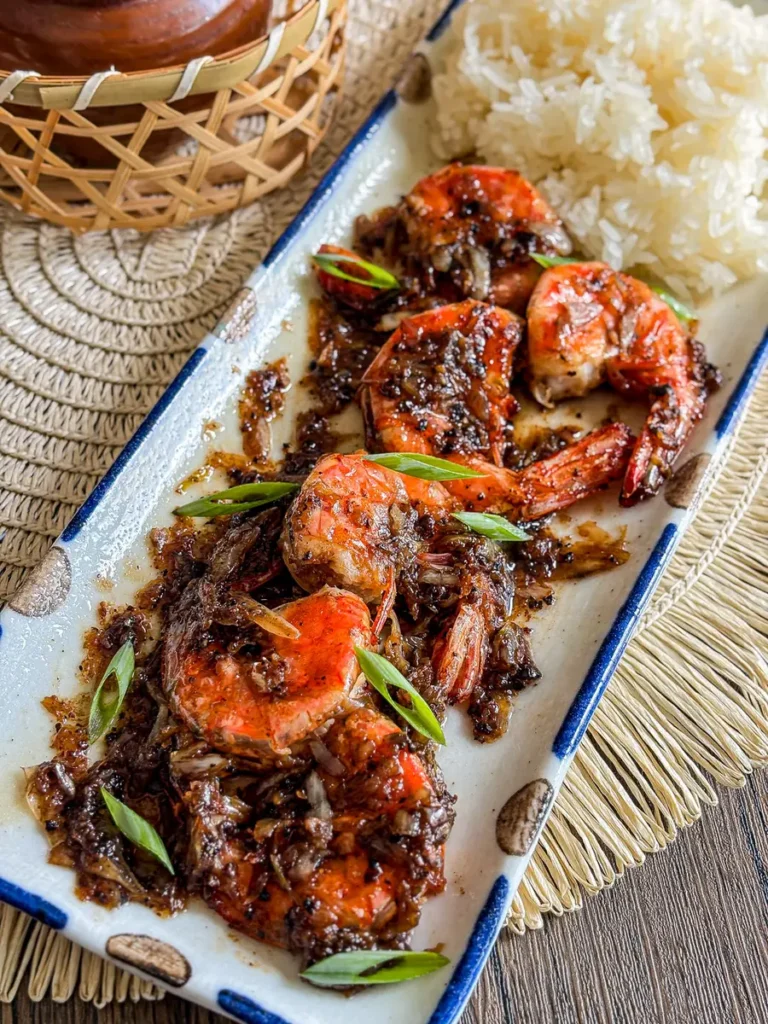 Thai garlic pepper shrimp with caramelized garlic and black pepper served with sticky rice on a ceramic plate.