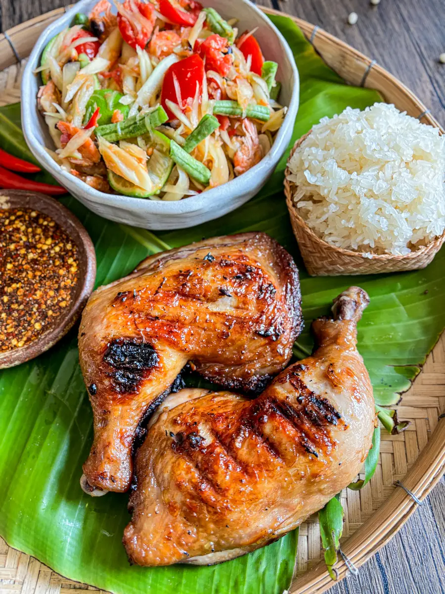 Thai gai yang grilled chicken with crispy skin, served with sticky rice, som tum, and nam jim jaew.