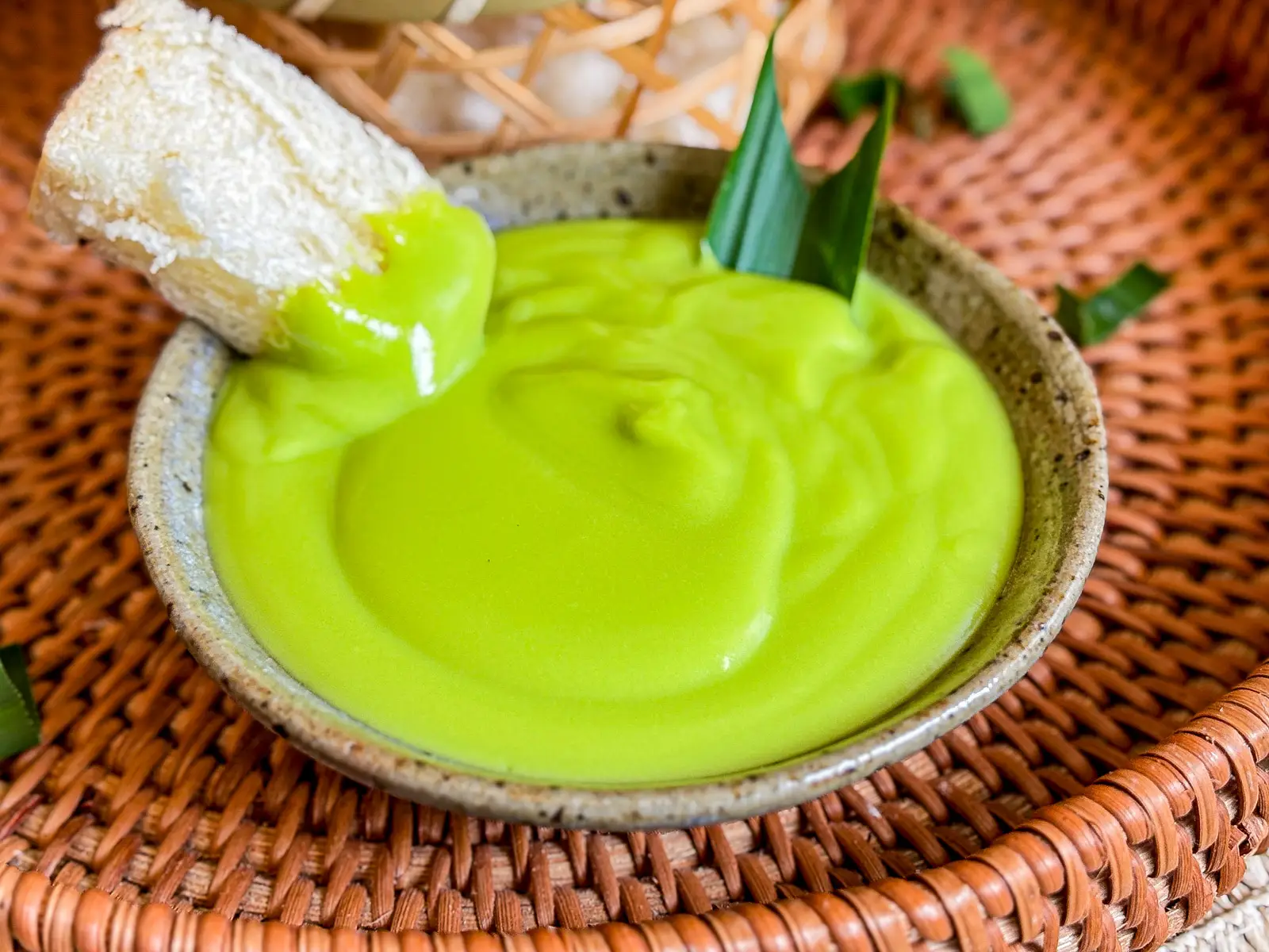 Thai pandan custard served in a ceramic bowl with a smooth, glossy texture, topped with pandan leaves and paired with soft white bread.