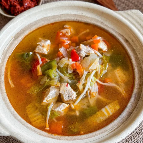 Thai red curry chicken soup served in a clay pot, filled with tender chicken, vegetables, and a light spicy broth.