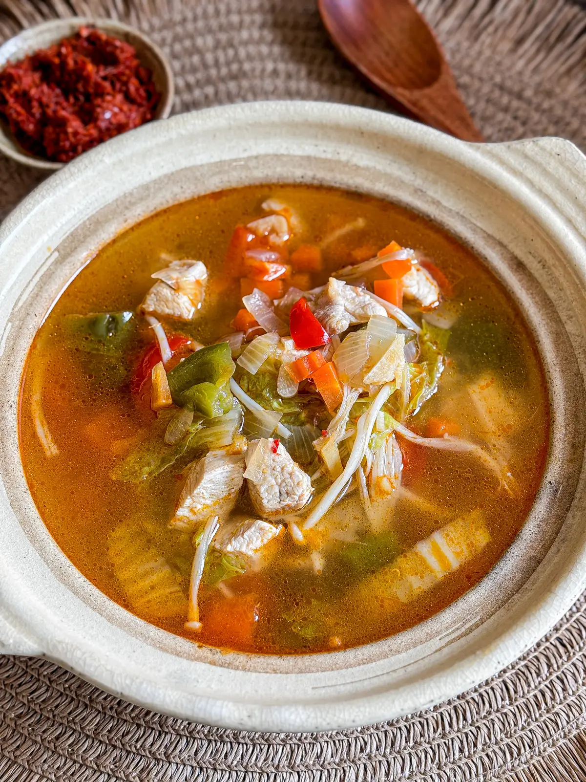 Thai red curry chicken soup served in a clay pot, filled with tender chicken, vegetables, and a light spicy broth.