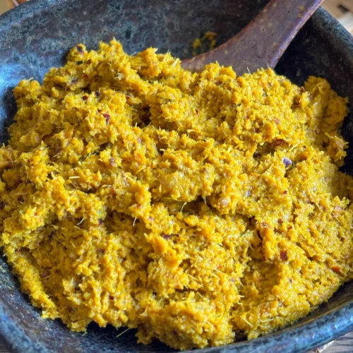 Homemade Thai yellow curry paste in a stone mortar, showing a coarse texture and vibrant golden color from fresh spices.