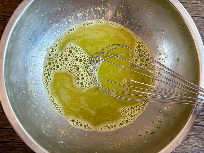 Pandan juice whisked with eggs, sugar, and coconut milk in a mixing bowl until fully combined and lightly foamy.