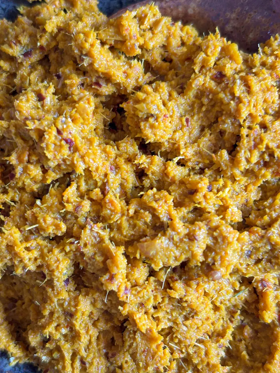 Close-up of yellow curry paste with a thick, fibrous texture, highlighting freshly pounded herbs and spices.