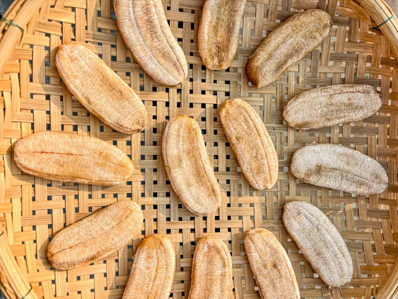Partially dried bananas flattened on a bamboo tray.