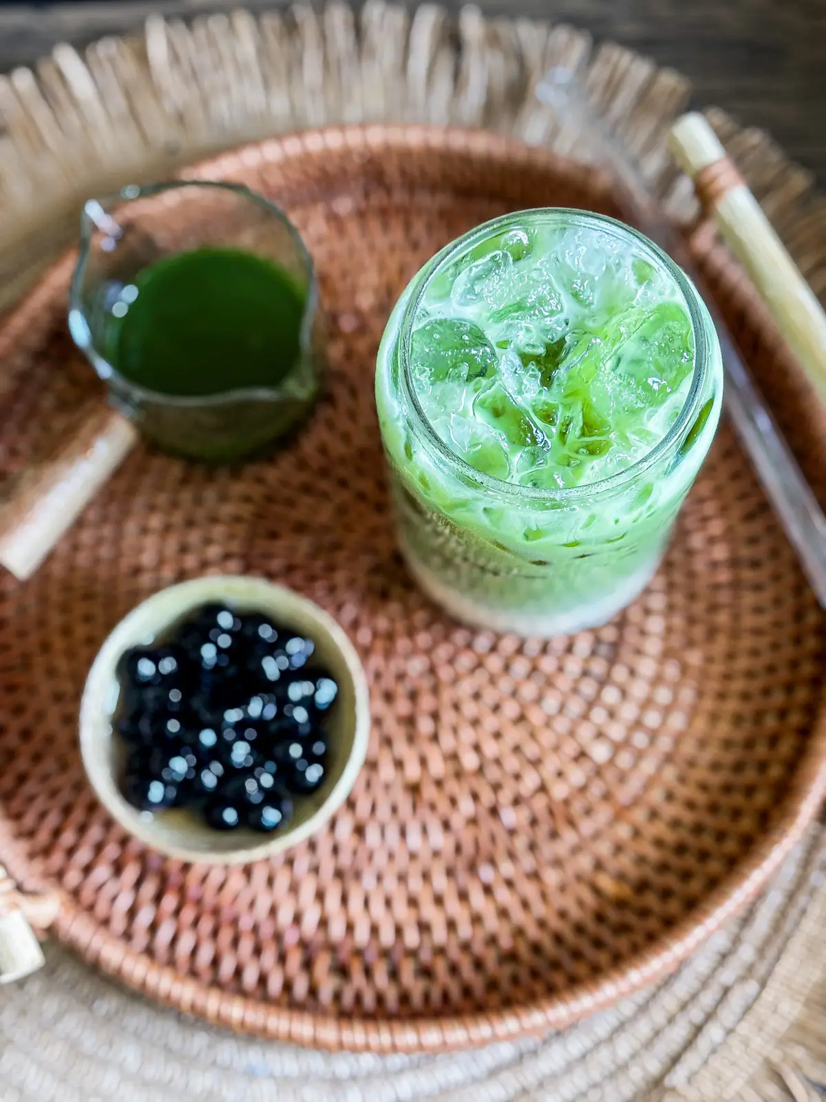 Thai green bubble tea with black boba pearls and ice served on a woven tray.