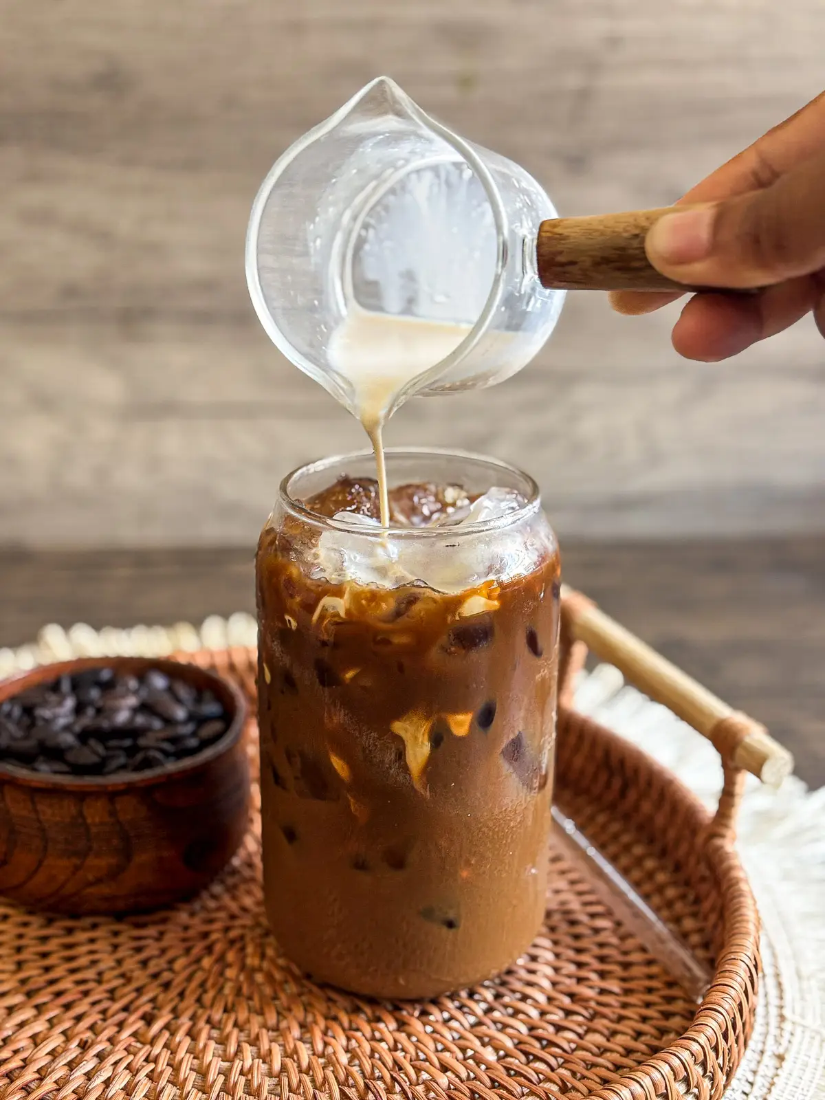Pouring milk into homemade Thai iced coffee with ice in a glass jar.