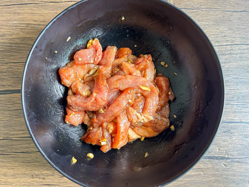 Sliced pork marinating with garlic and sauce in a bowl.