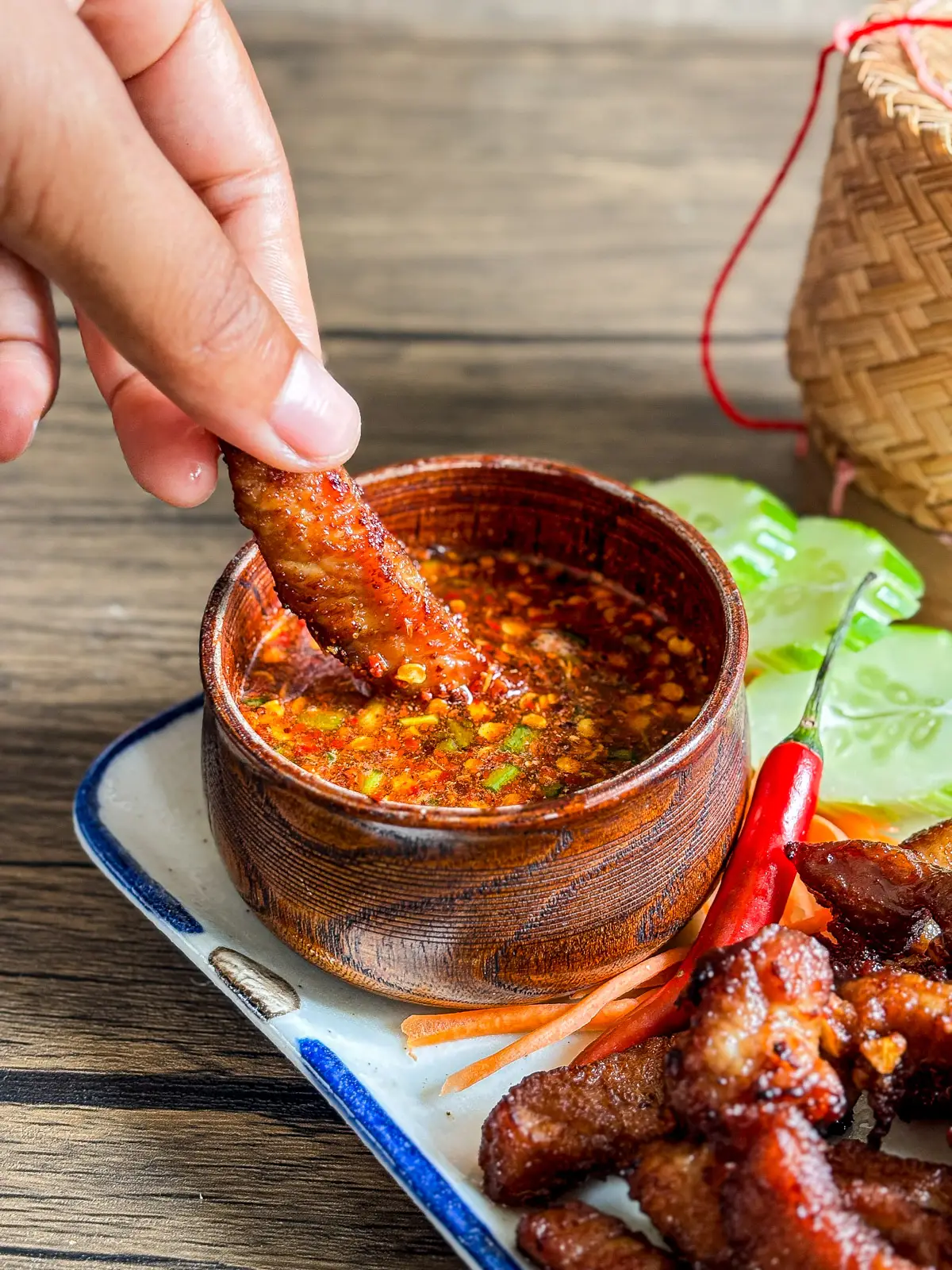 hand dipping moo tod, Thai fried pork into a spicy chili sauce.