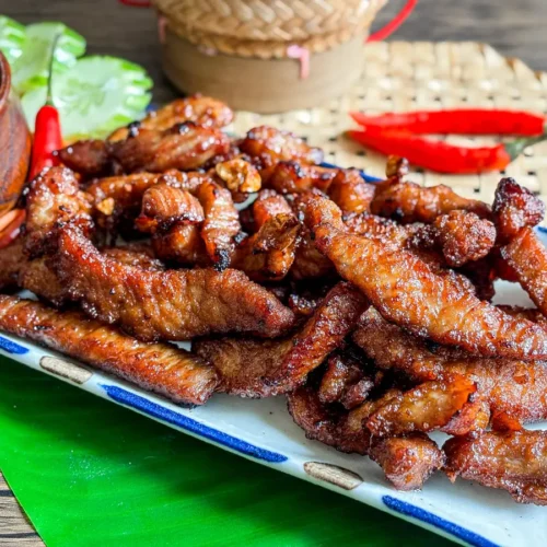Close-up of plate of crispy Thai fried pork served with chili dipping sauce.