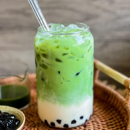 Thai green tea boba with tapioca pearls and ice in a glass jar with a glass straw.