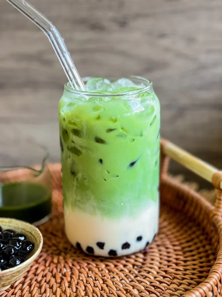 Thai green tea boba with tapioca pearls and ice in a glass jar with a glass straw.