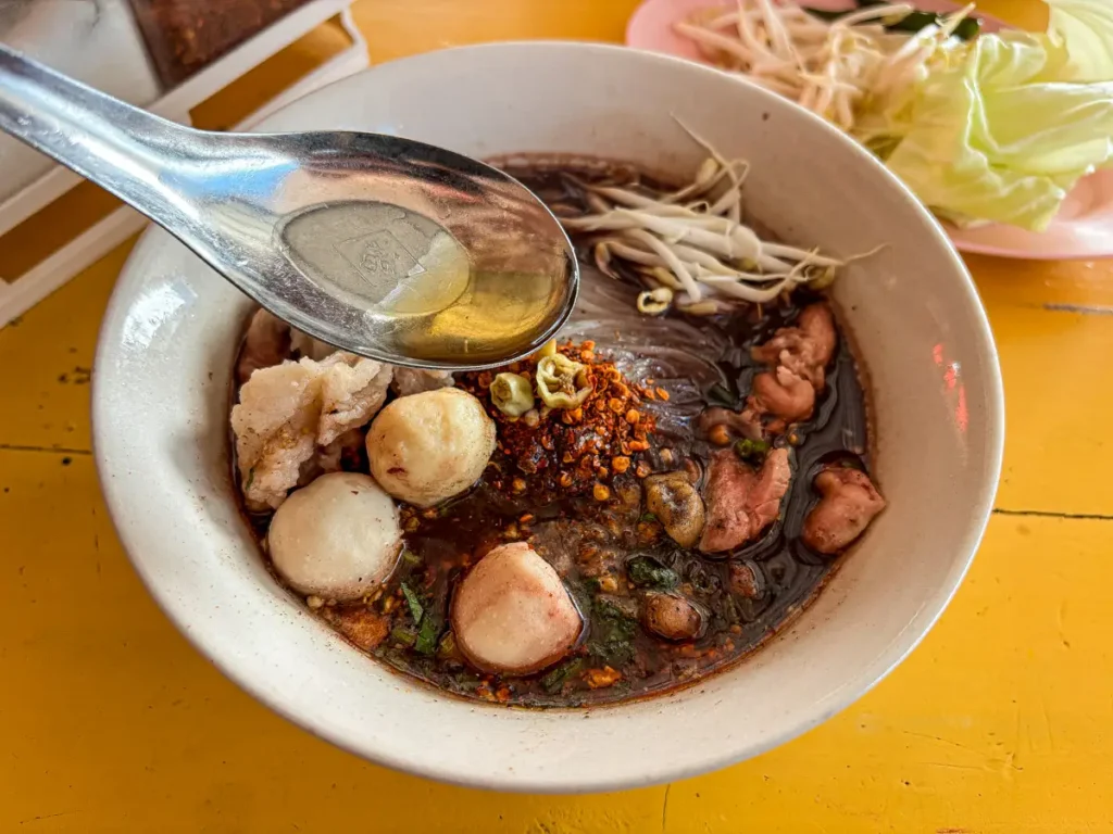 Adding fish sauce to season Thai noodle soup.